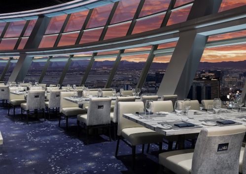 Elegant restaurant interior with large windows showcasing a sunset view over a city skyline.